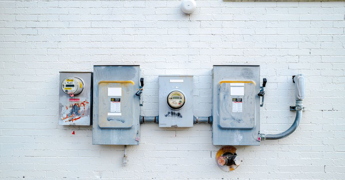 Electrical boxes and power meters mounted on a white brick wall.