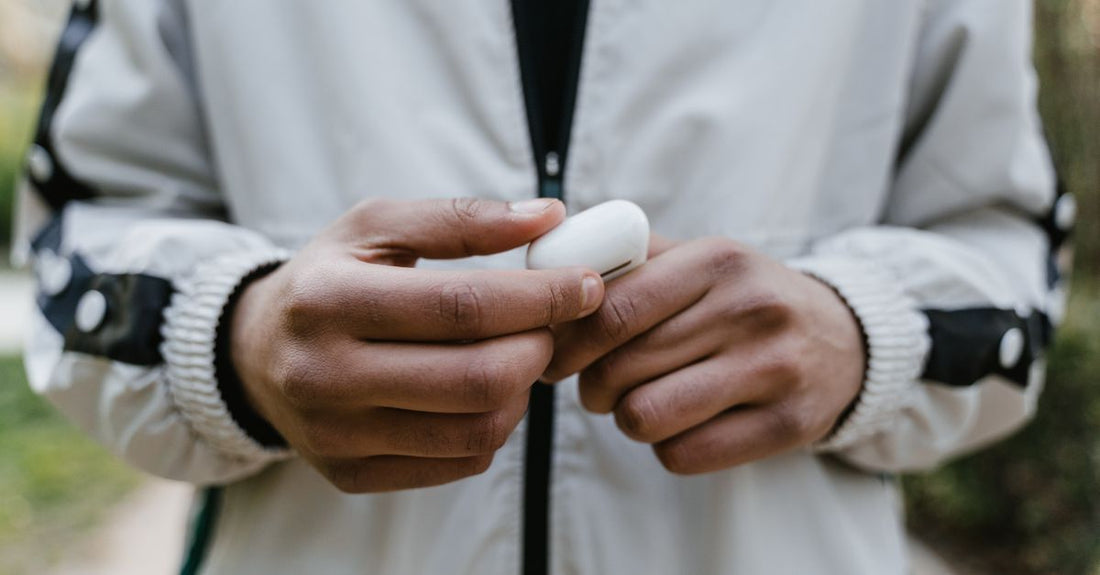 A person in a jacket holding a case of wireless earbuds outdoors.